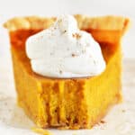 A slice of pumpkin pie with condensed milk on a white plate.