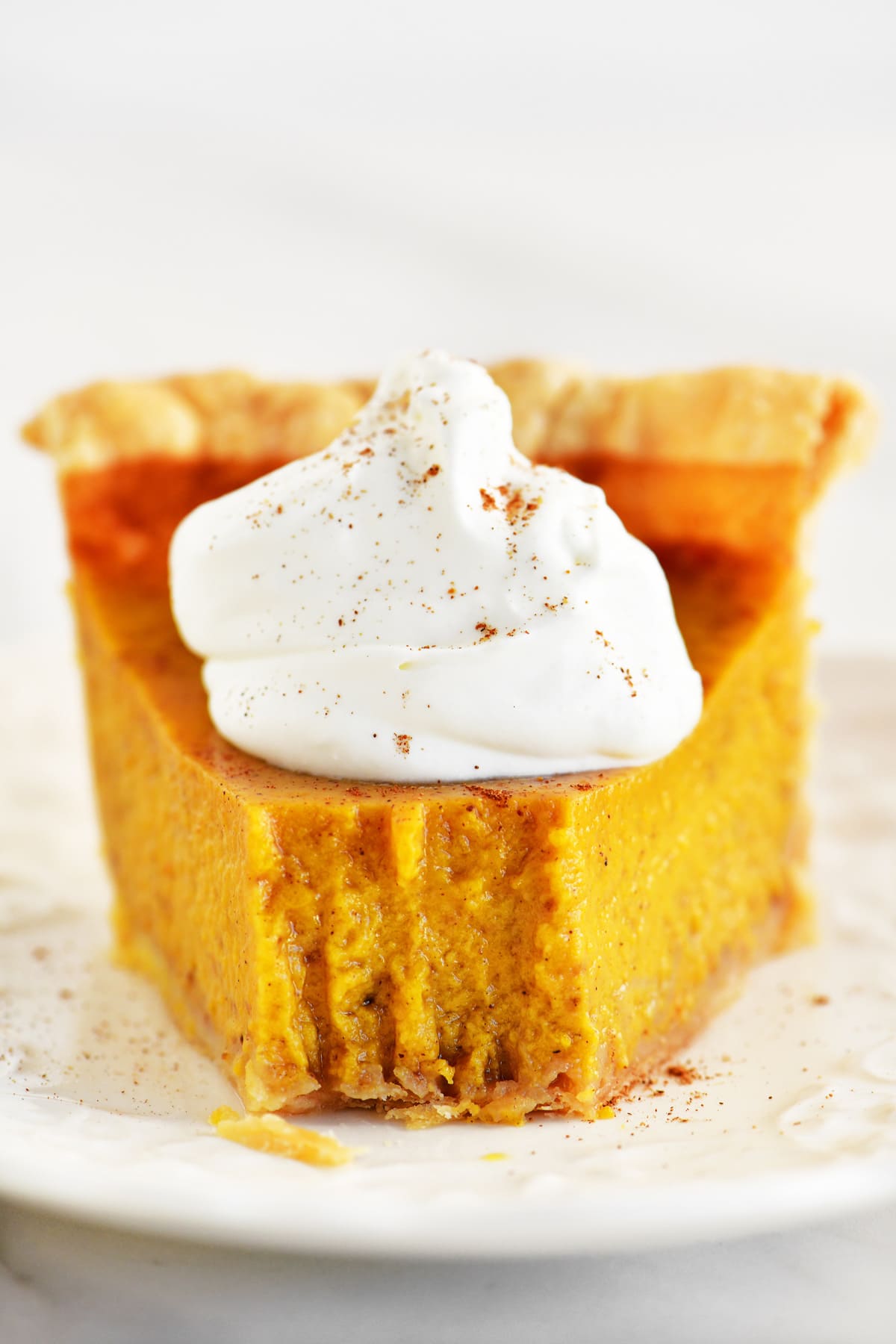 A slice of pumpkin pie with condensed milk on a white plate.