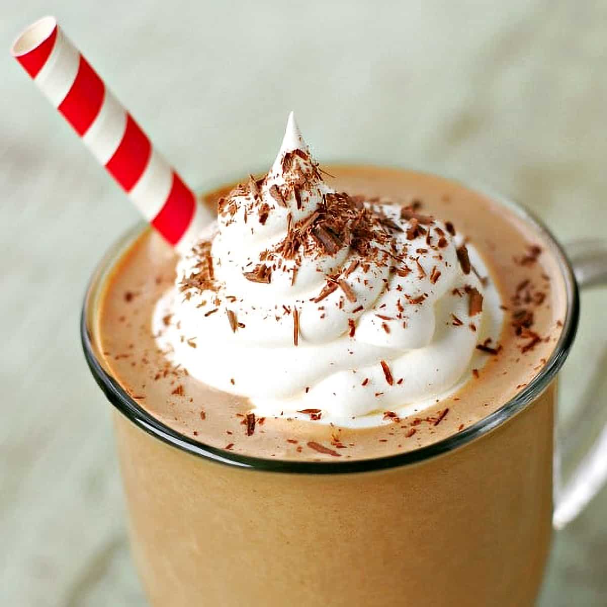 Chocolate shavings and whipped cream on top of Frosty Mocha punch in a glass with a straw.