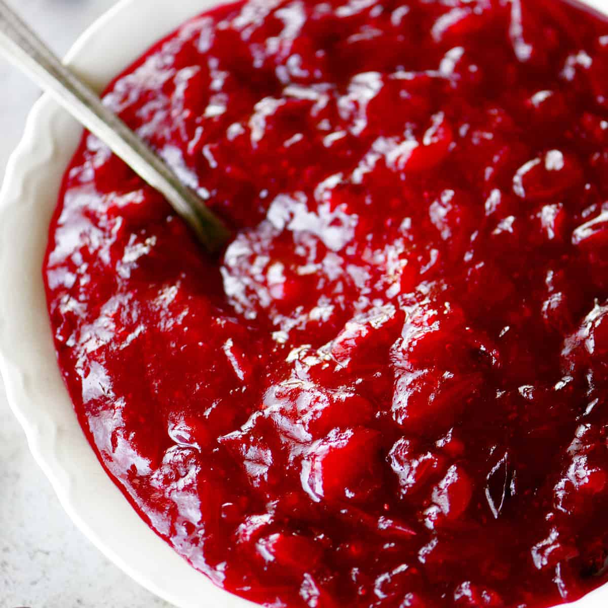 Homemade cranberry sauce in a white bowl with a spoon.
