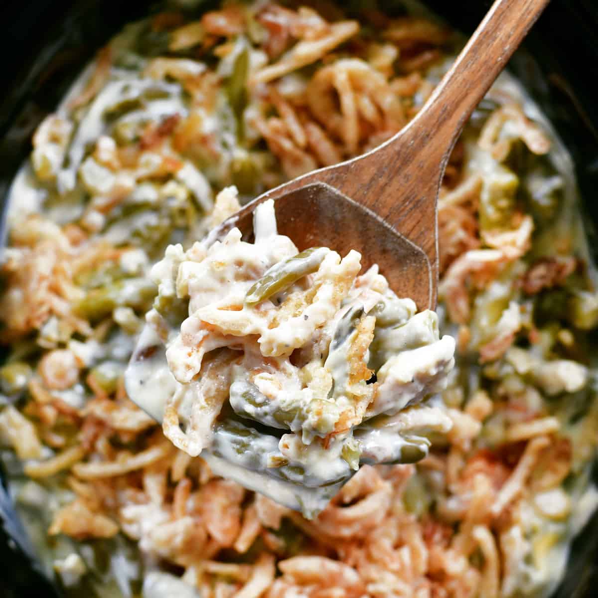 A wooden spoon with green bean casserole in it.