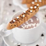 Chocolate chips biscotti on a white mug of hot chocolate.