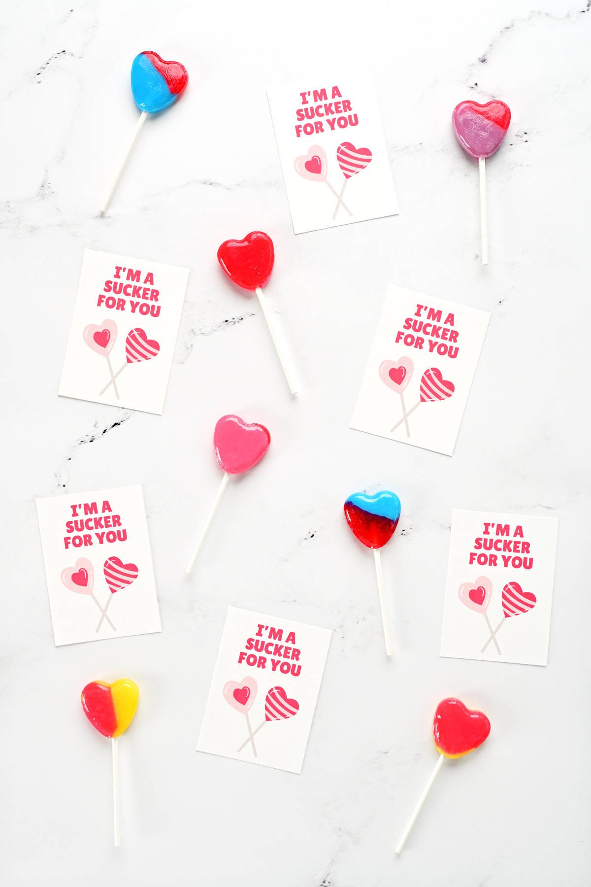 Printable valentine cards for kids on a countertop with heart shaped lollipops.