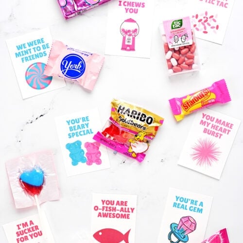 Assorted candies and free printable valentine cards for kids on a countertop.