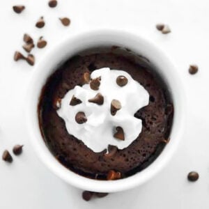 A chocolate mug brownie in a cup with whipped cream and chocolate chips.