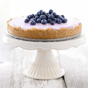 A no bake blueberry cheesecake on a white cake stand.