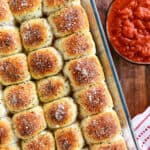 Pepperoni rolls in a baking dish next to a bowl of dipping sauce.