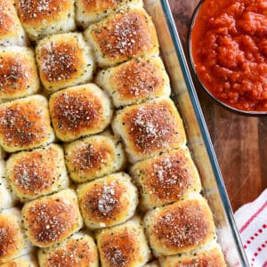 Pepperoni rolls in a baking dish next to a bowl of dipping sauce.