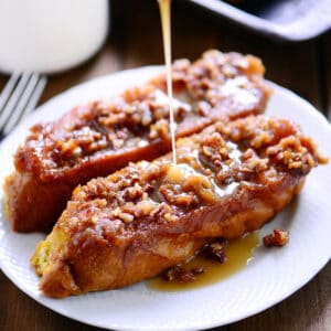 Drizzling syrup on pumpkin pecan French toast on a white plate.
