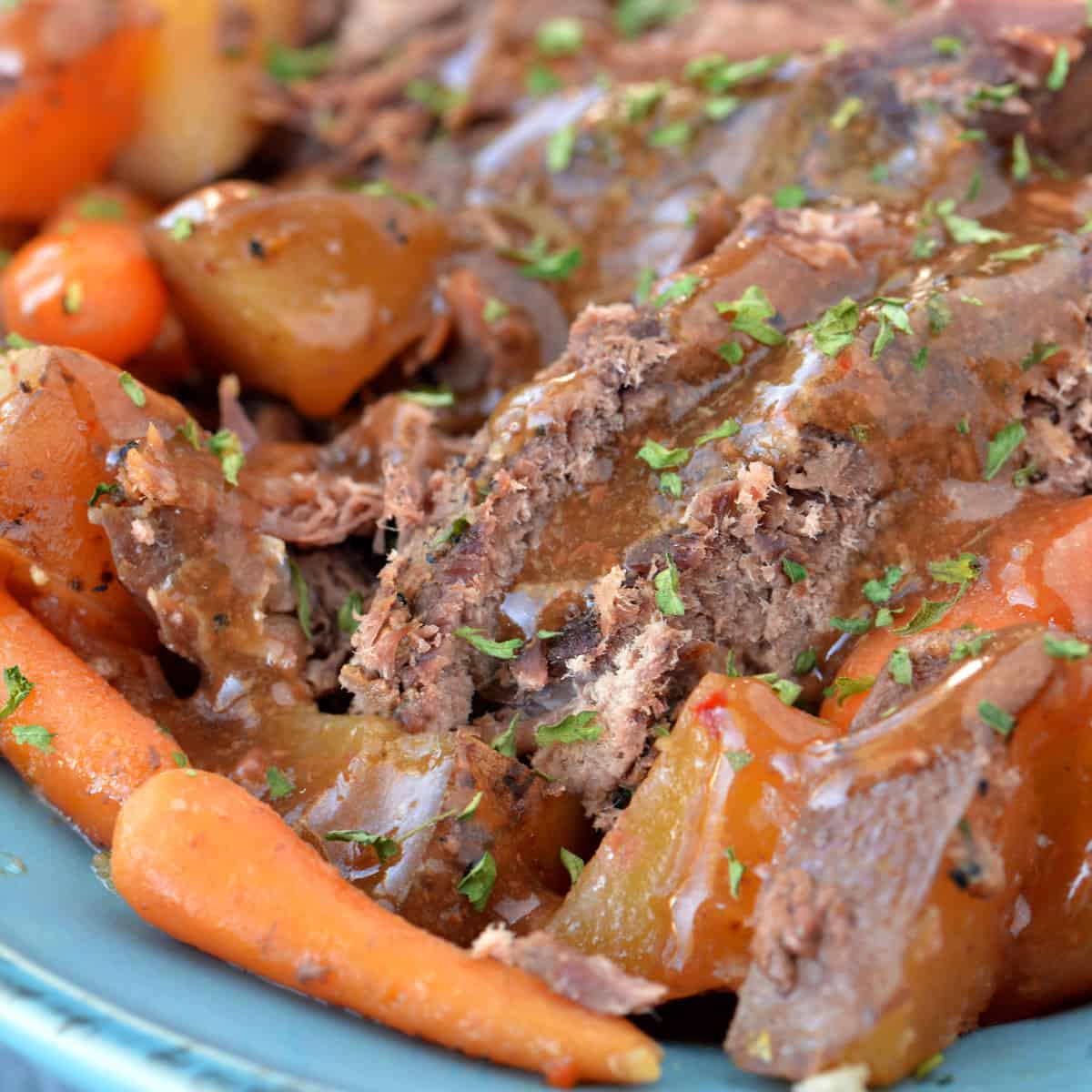 Slow cooker roast beef with potatoes and carrots on a blue platter.