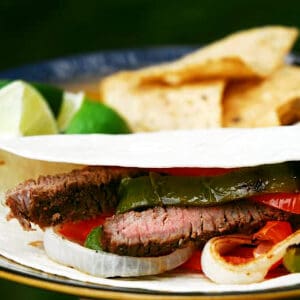 A fajita on a plate with chips and lime slices.