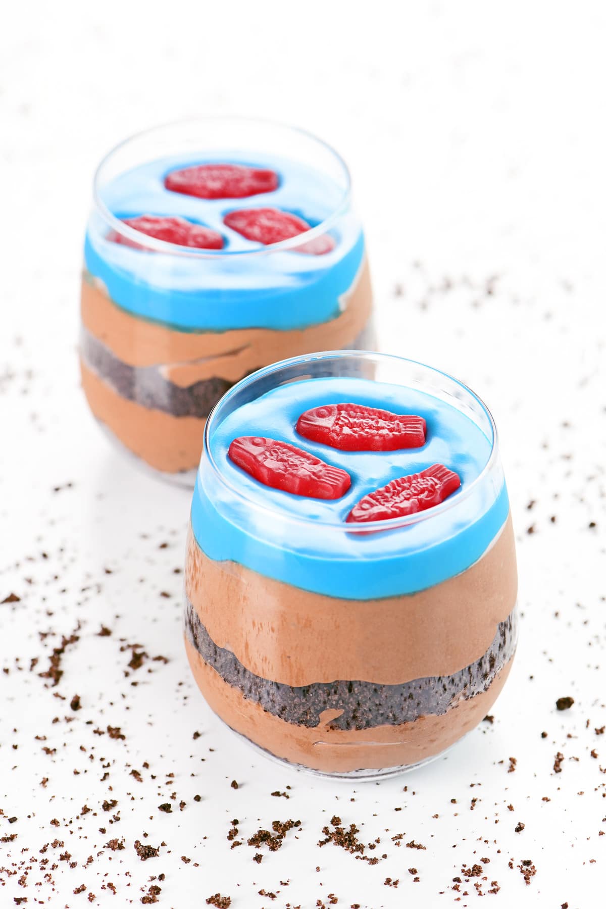 Dirt cake cups with a blue frosting lake and red gummy fish on top.