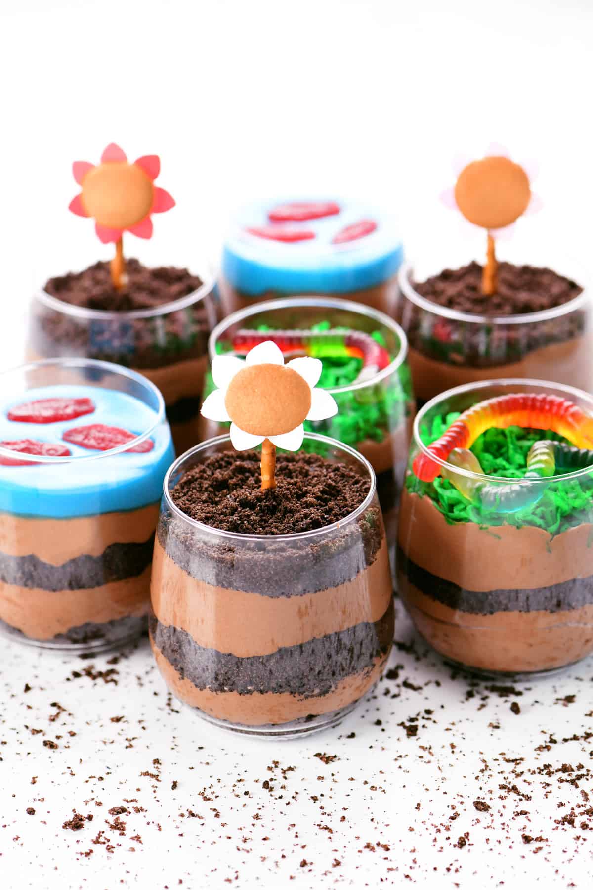 Chocolate pudding dirt cake cups topped with Oreos, gummy fish, gummy worms, and edible flowers.