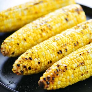 Four ears of grilled corn on the cob on a black serving platter.