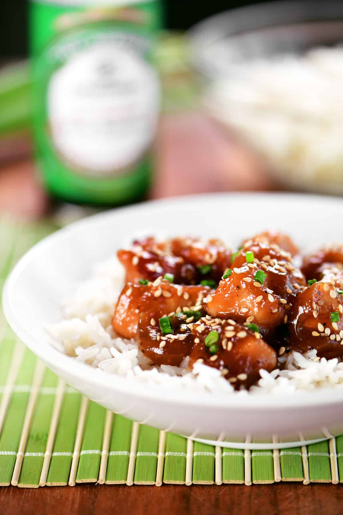 Slow cooker honey sesame chicken over rice in a white bowl on a green mat.