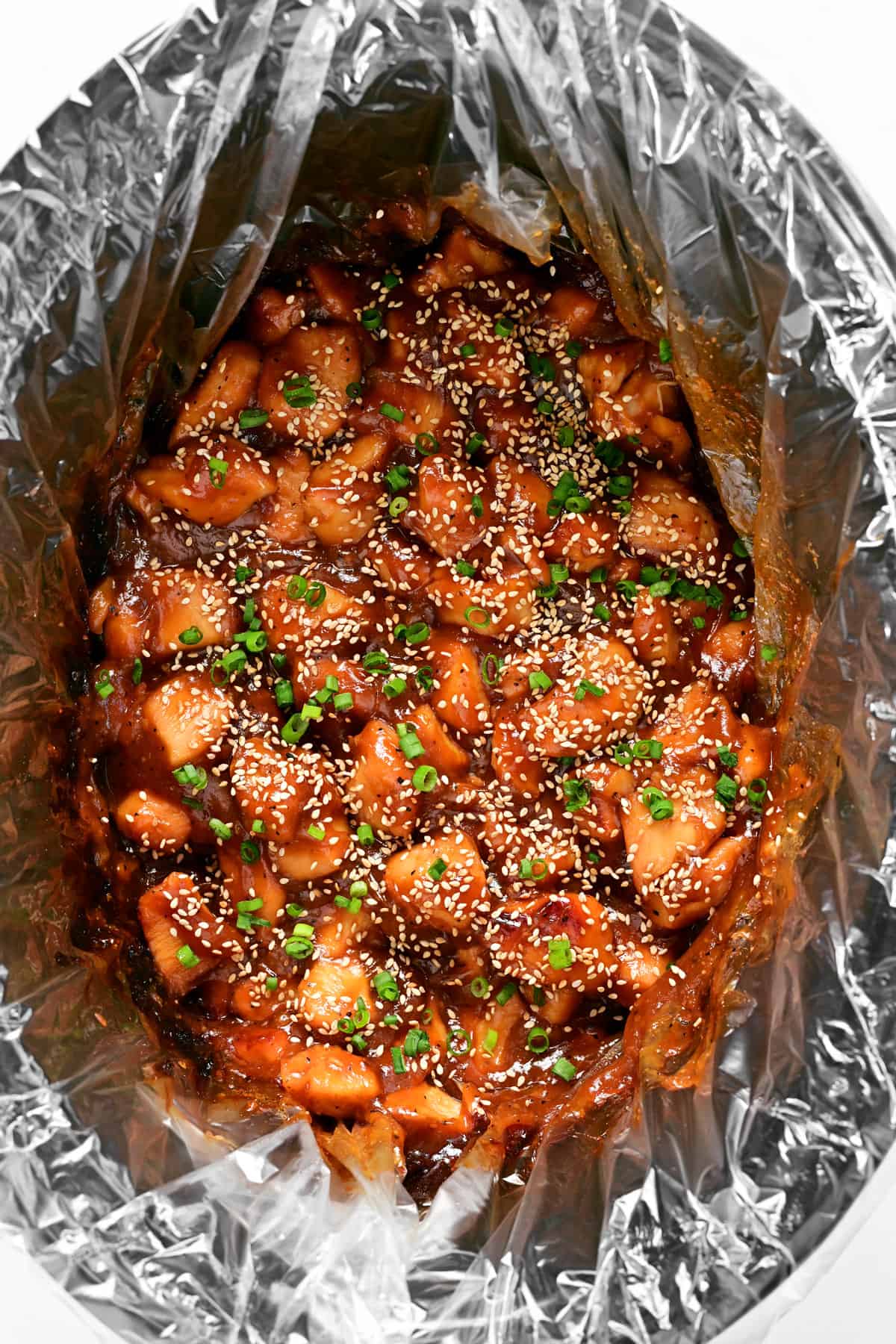 Slow cooker honey sesame chicken in a crockpot garnished with green onions.