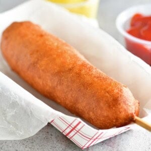 A homemade corn dog in a paper tray.