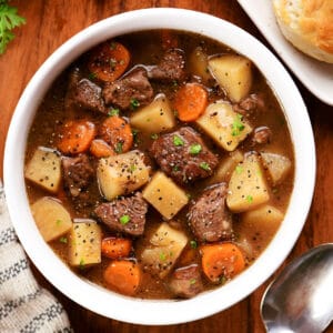 Slow cooker beef stew in a white bowl with biscuits on a tray.