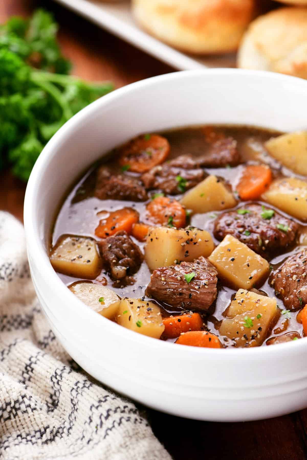 Slow cooker beef stew in a white bowl with biscuits on a tray.