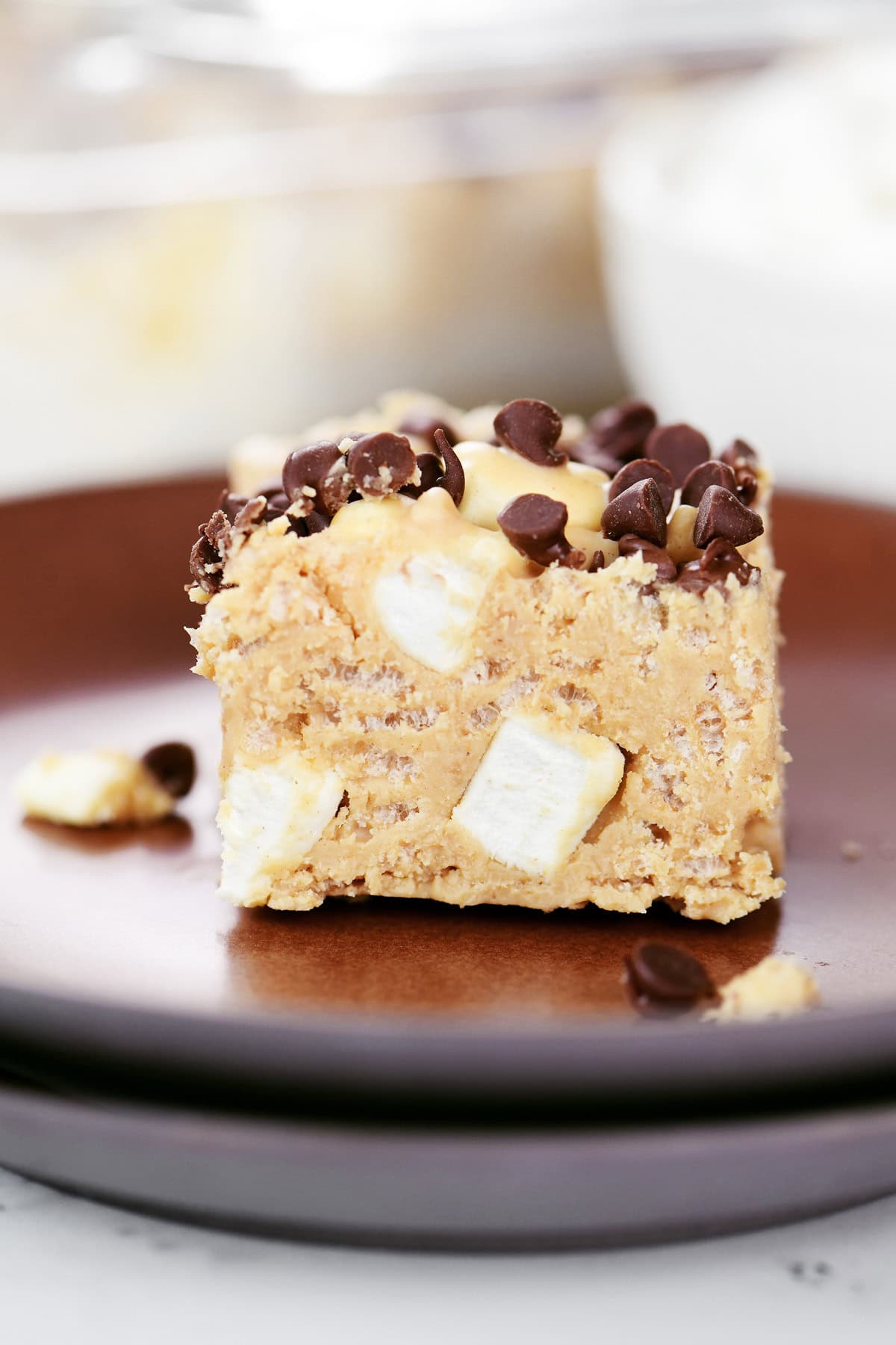 A crispy avalanche bark bar square with marshmallows and mini chocolate chips on a brown plate.