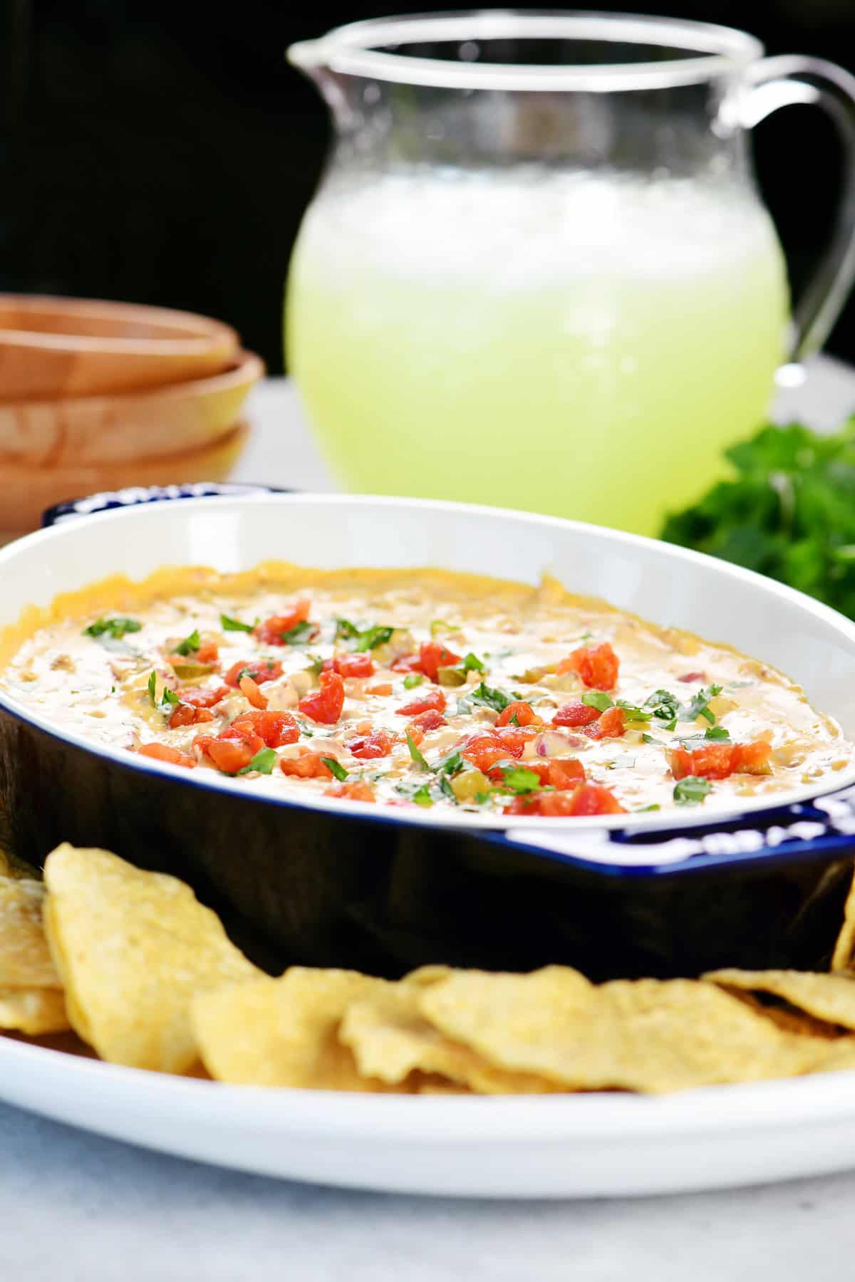 Sausage queso dip on a platter with chips and a pitcher of lemonade in the background.