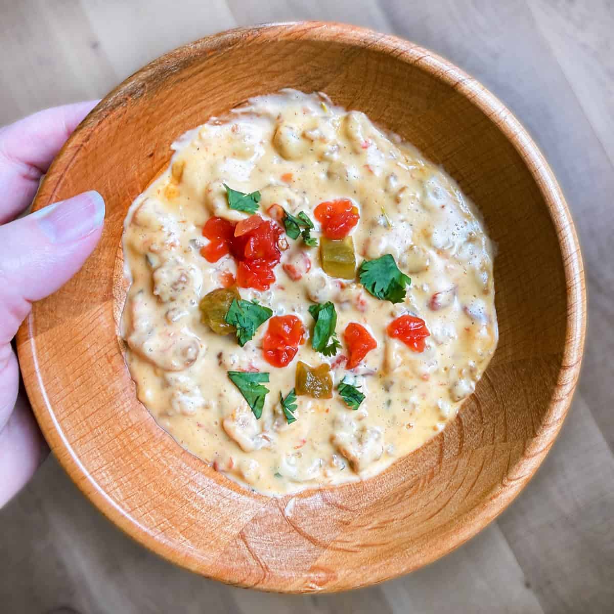 A hand holding a bow with sausage queso dip.