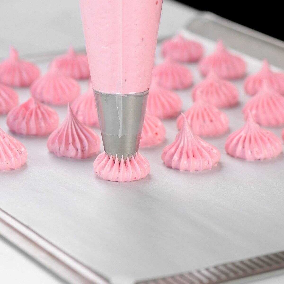 Piping strawberry meringue cookies onto parchment paper on a sheet pan.