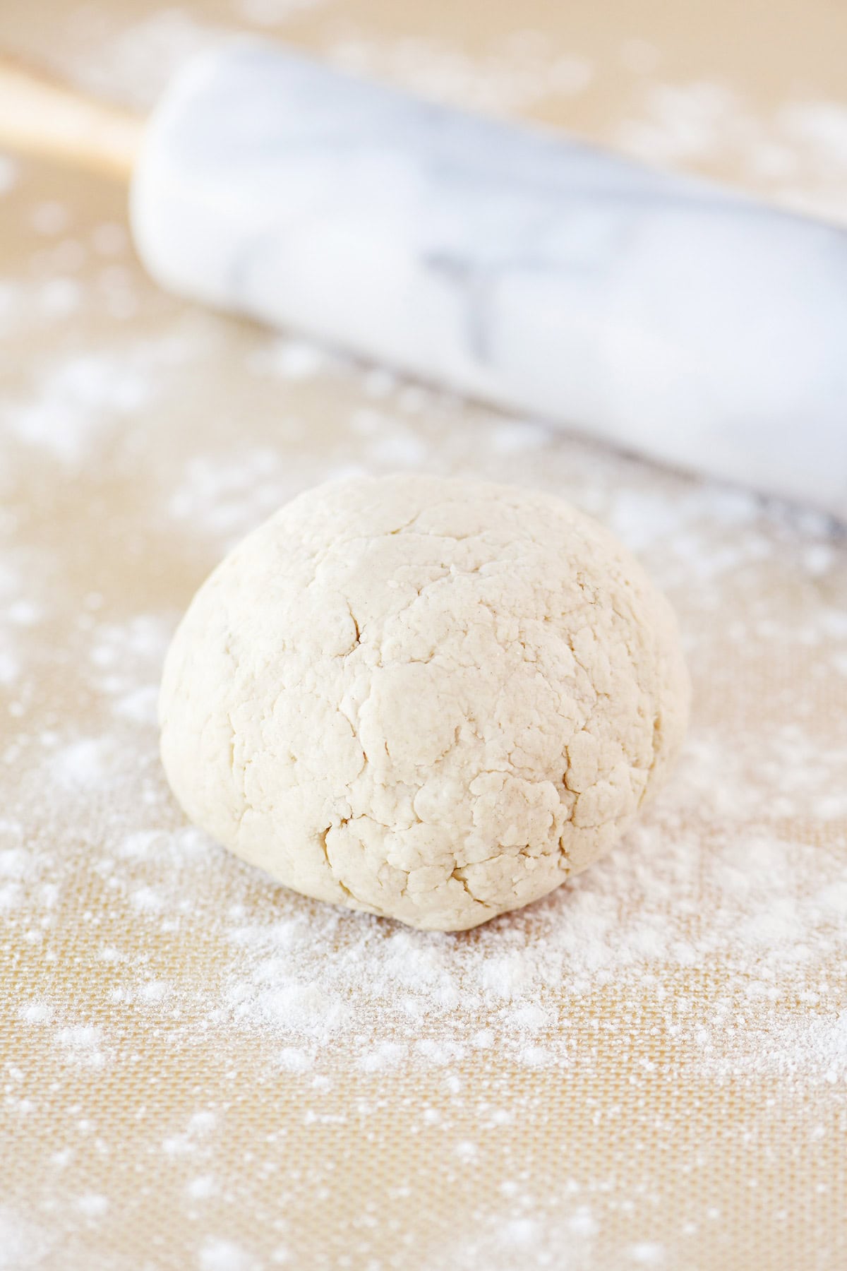 Blended cottage cheese dough ball on a floured surface with a marble rolling pin.