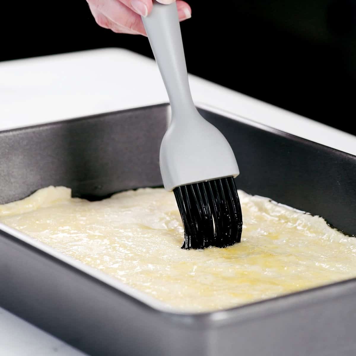 Brushing melted butter over dough in a pan.
