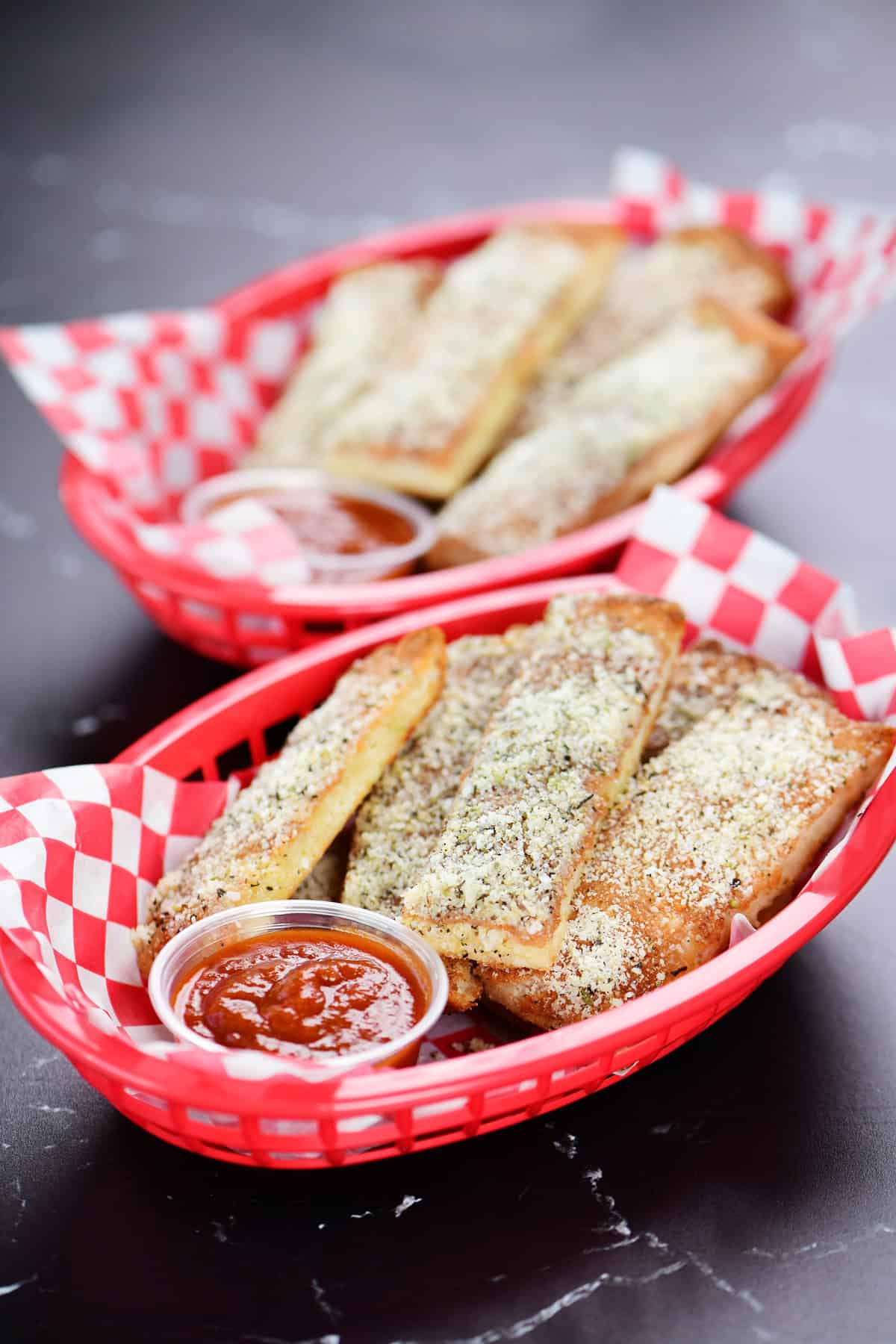 Cottage cheese breadsticks with parmesan on top in red plastic baskets with cups of sauce.