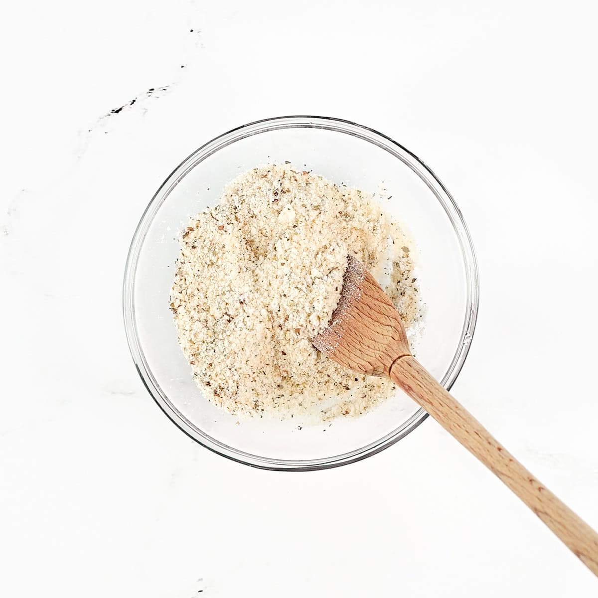 Seasoned Parmesan mixture in a small bowl with a small wooden spoon.