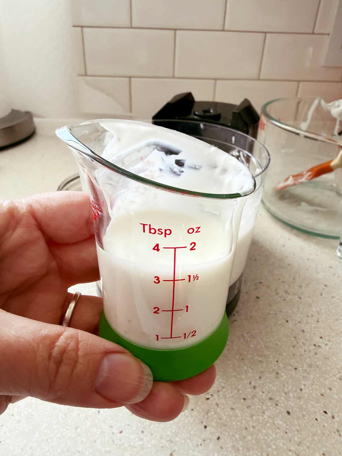 A hand holding a measuring cup of whey drained from cottage cheese.