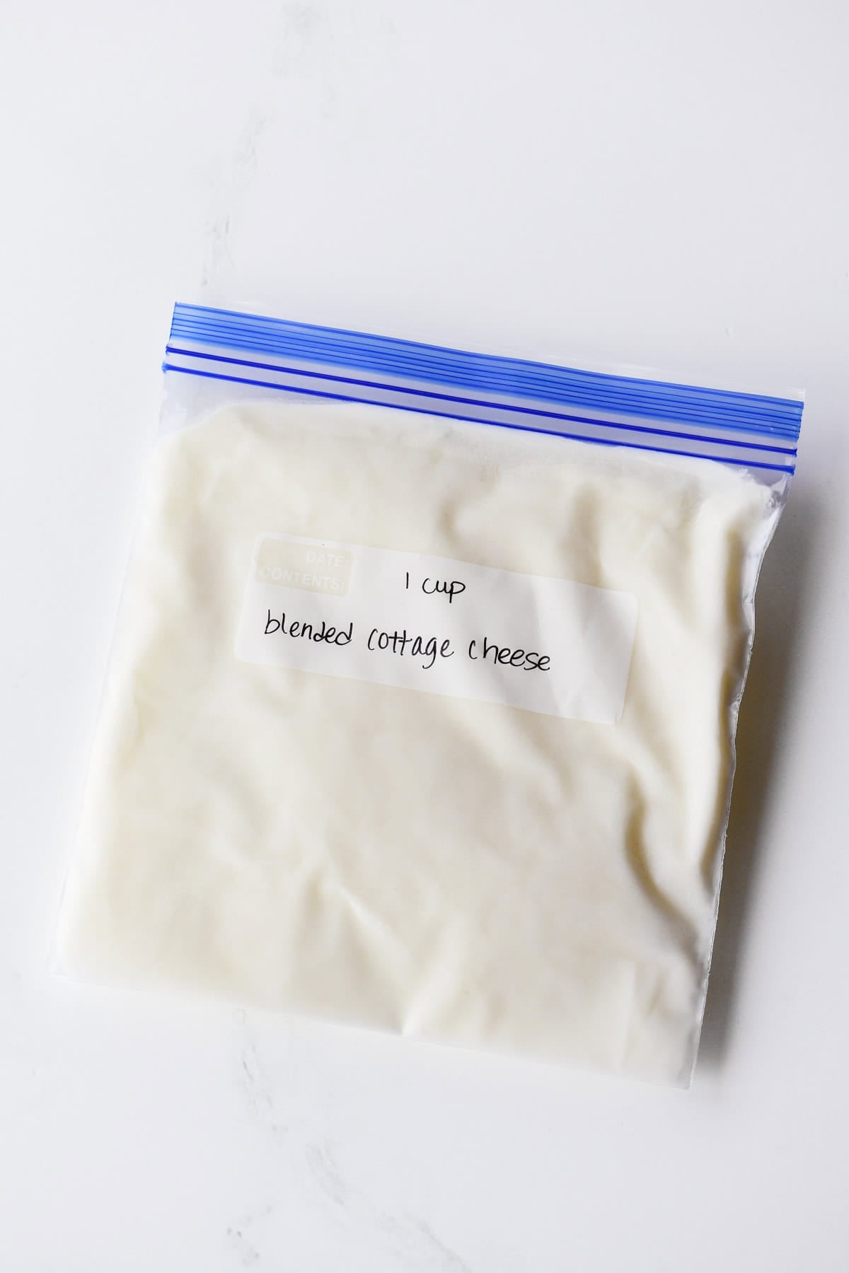 A quart size freezer bag with one cup of blended cottage cheese written on it.