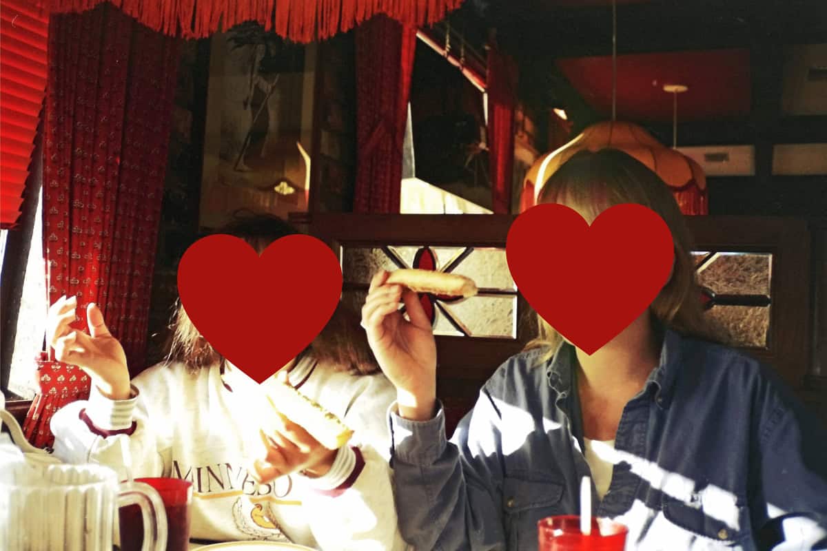 Two people in a restaurant with red hearts covering their faces.