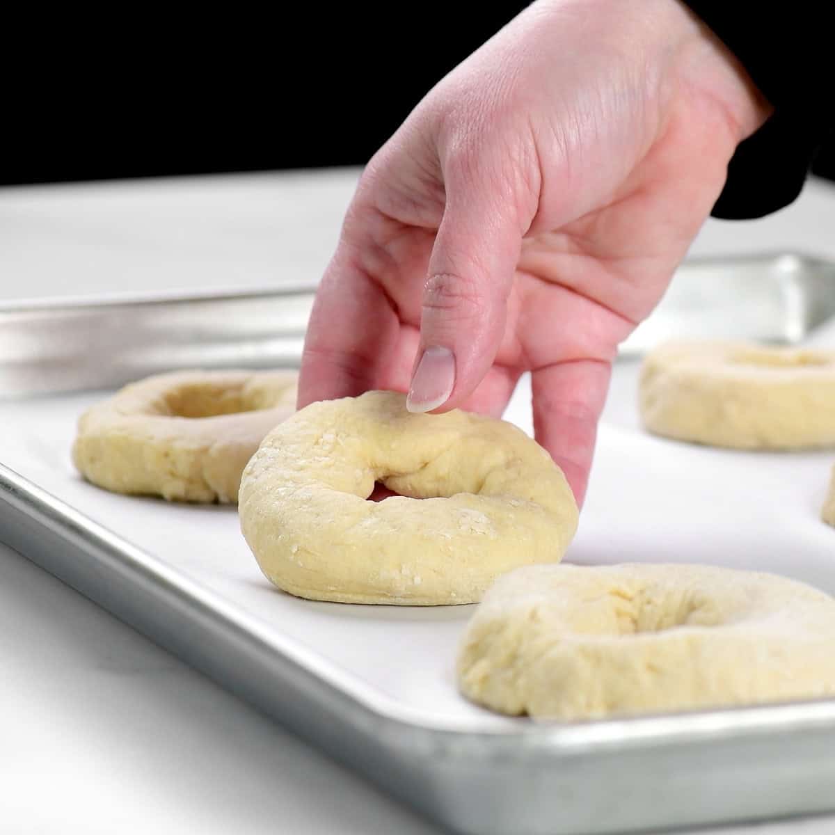 Setting a formed bagel on a baking sheet.