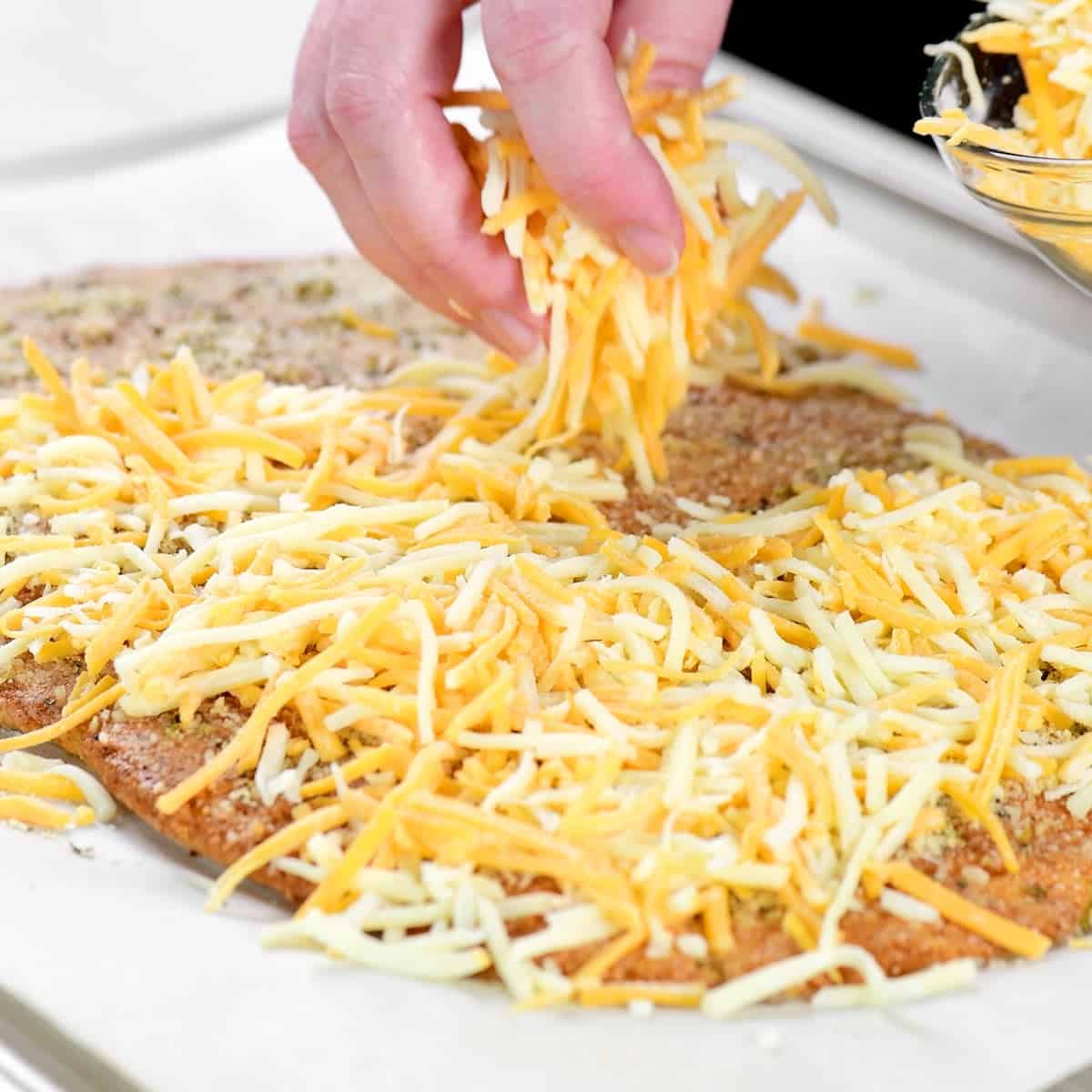 A hand sprinkling shredded cheese over the top.