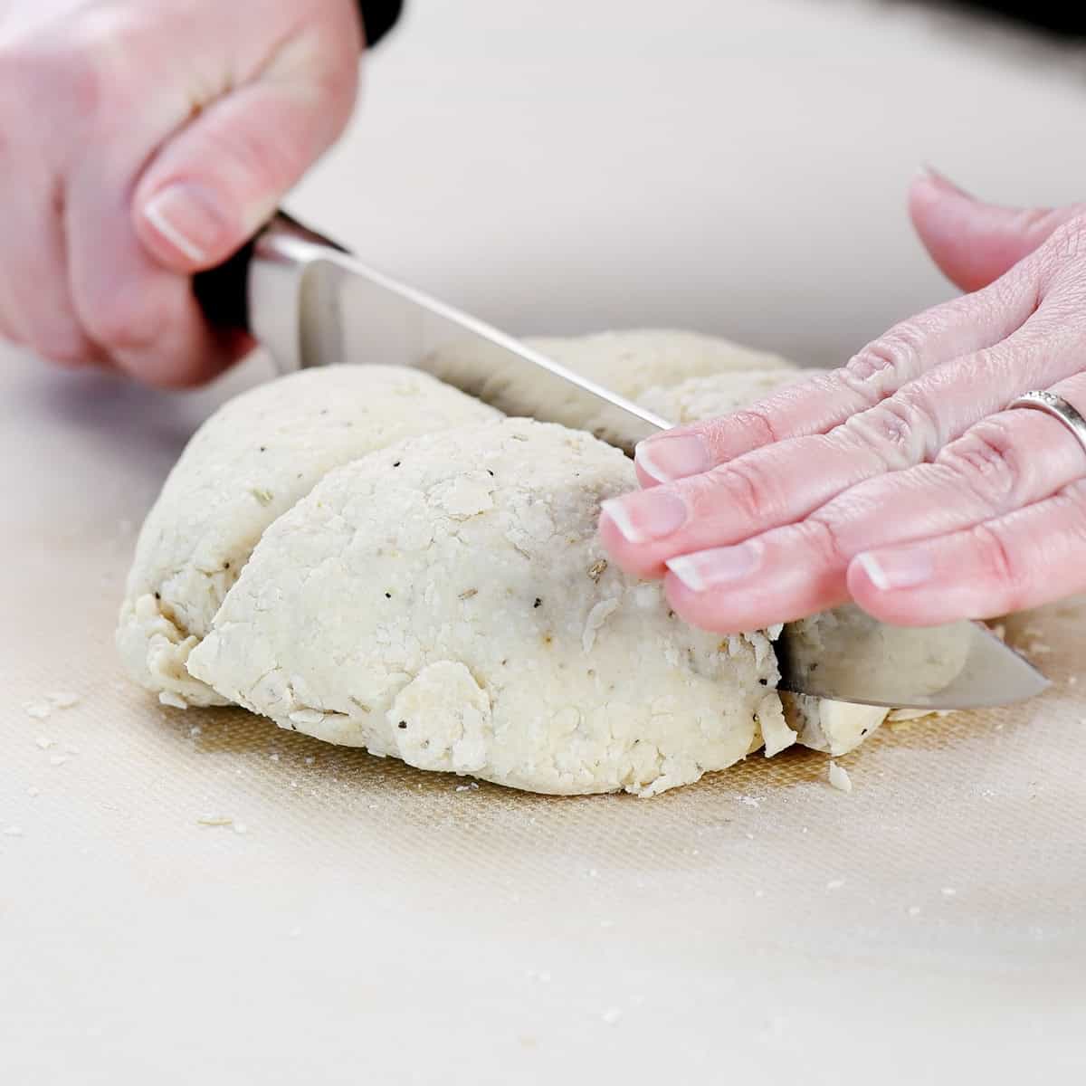 Hands cutting dough with a chef's knife.