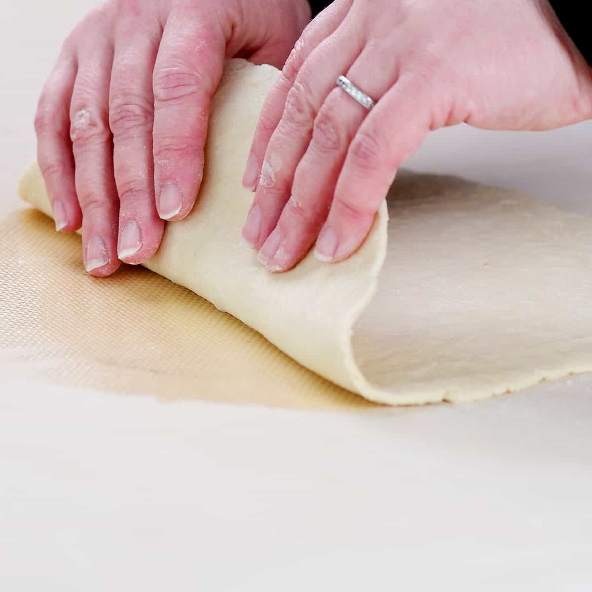 Hands lifting cottage cheese focaccia dough from a silicone mat.