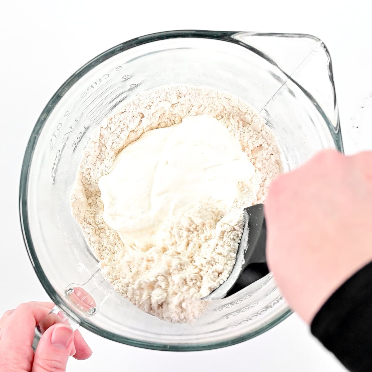 Stirring cottage cheese focaccia dough in a glass bowl.