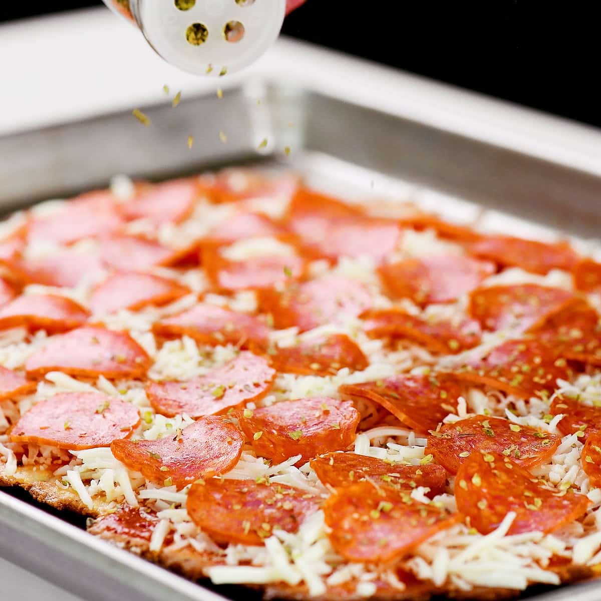 Sprinkling Italian seasoning on the unbaked pizza.