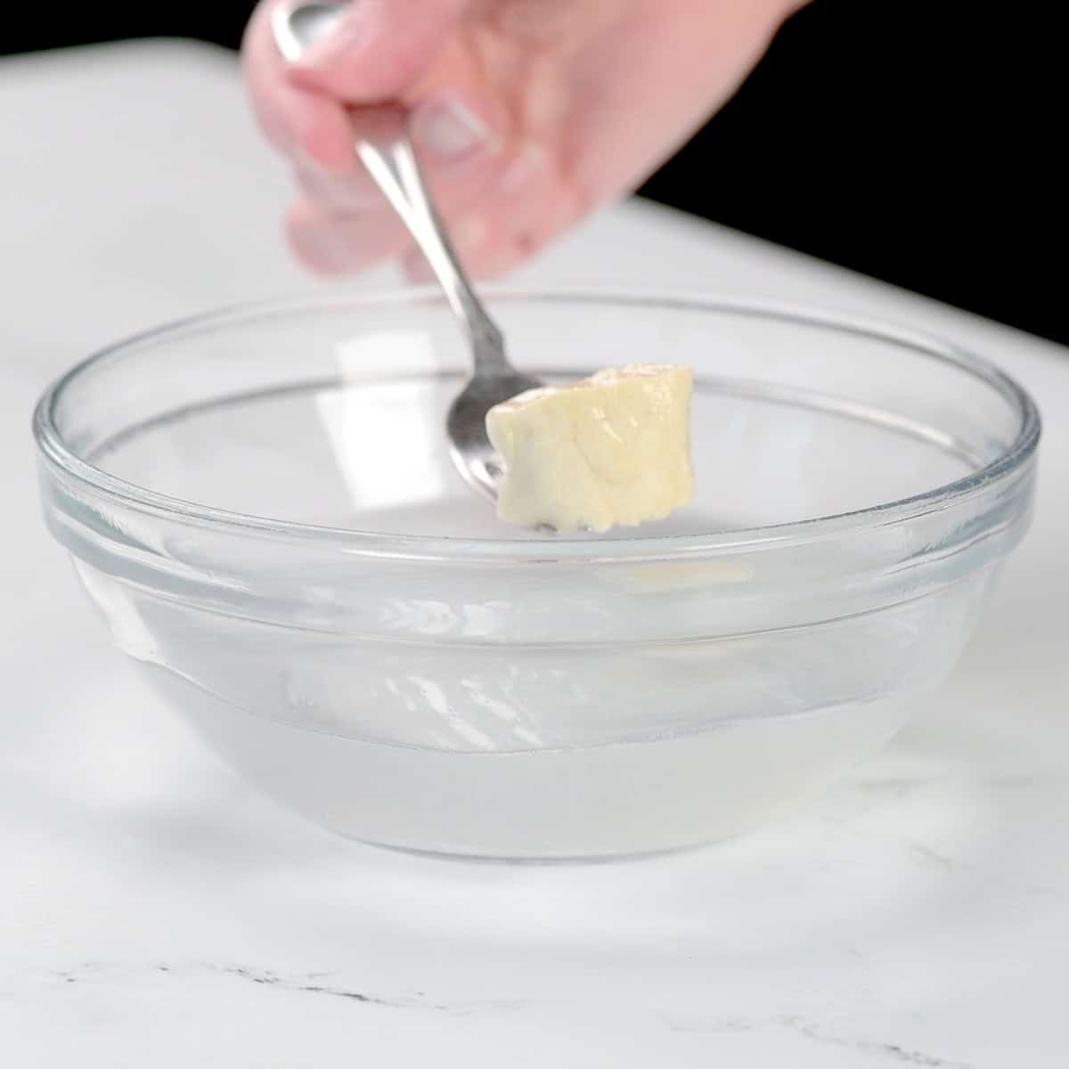 A piece of dough on a fork over a bowl of baking soda water.