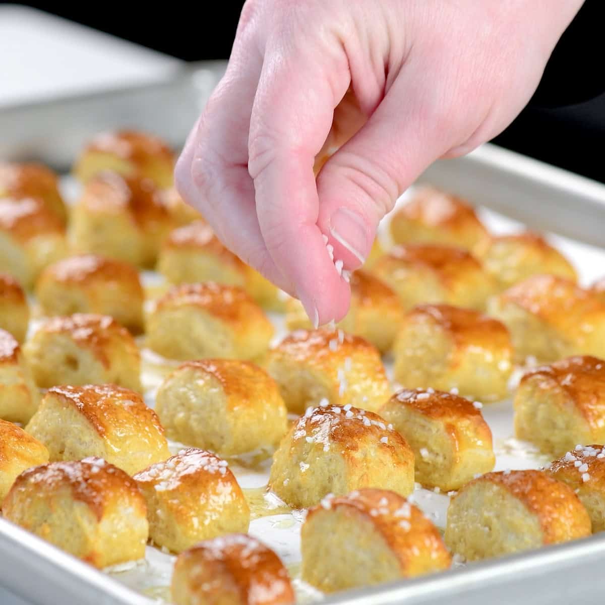 Sprinkling salt on baked cottage cheese pretzel bites.
