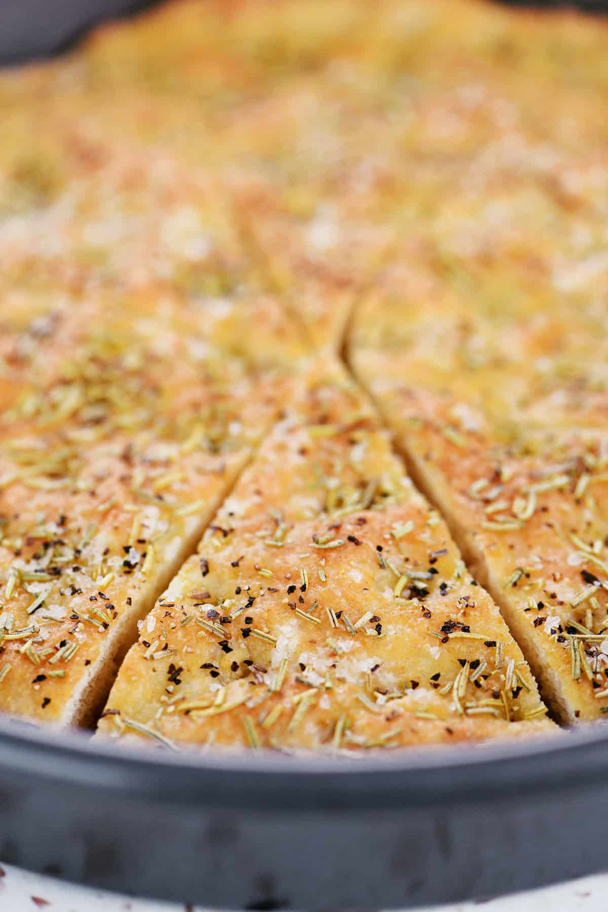 A round pan holding sliced cottage cheese focaccia with rosemary, black pepper, and sea salt.