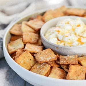 Seasoned, crispy cottage cheese crackers in a round tray with a bowl of dip in the middle.