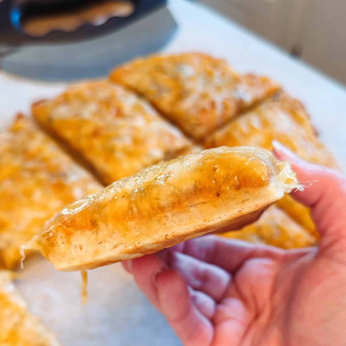 A hand holding a slice of cottage cheese cheesy bread.