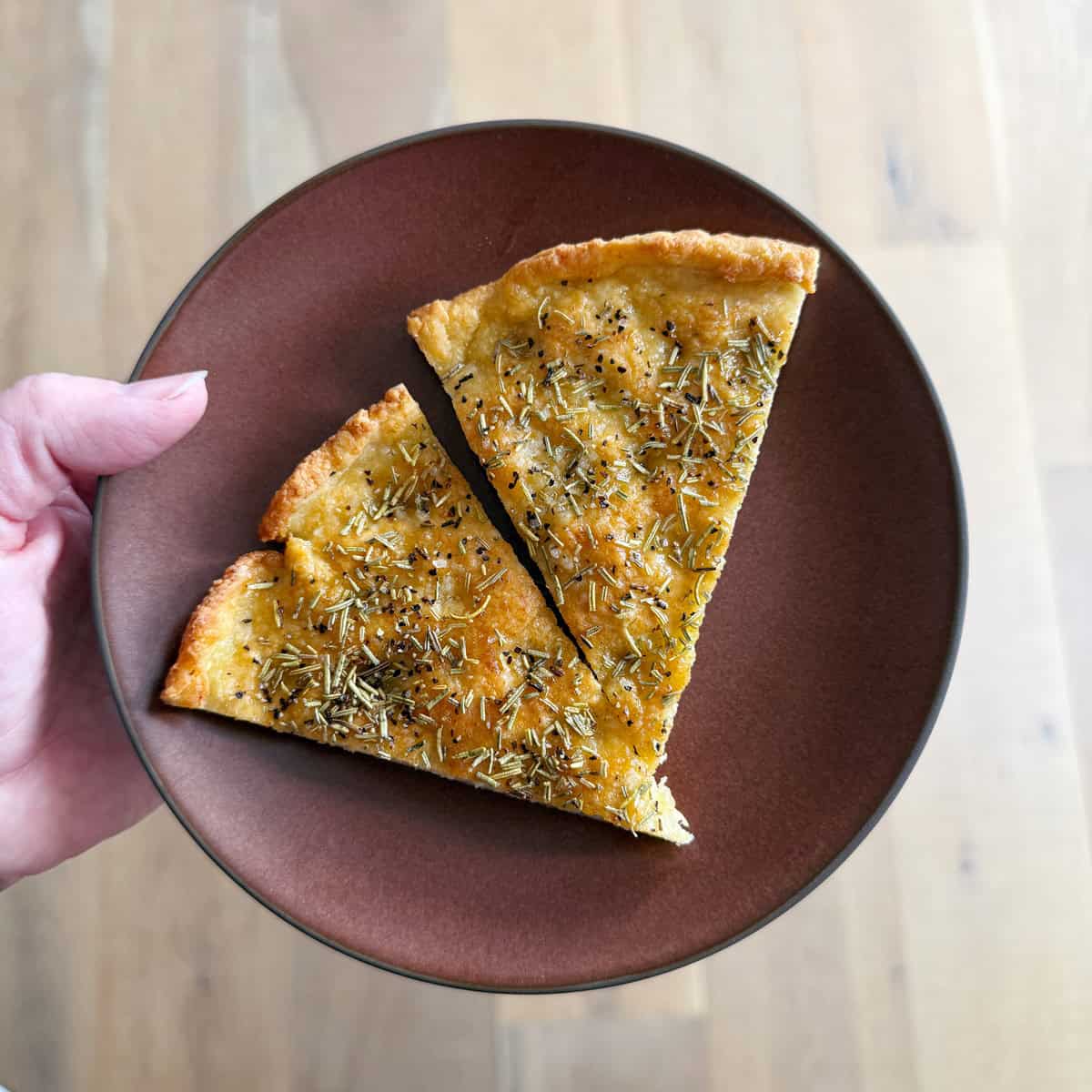 A hand holding a brown plate with two slices of cottage cheese focaccia.