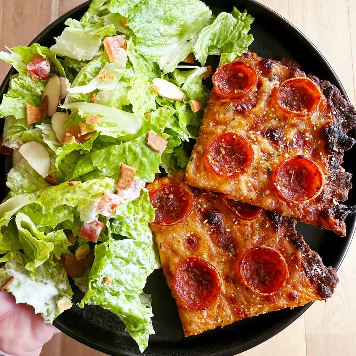 A hand holding a plate with two slices of cottage cheese pizza and a salad.