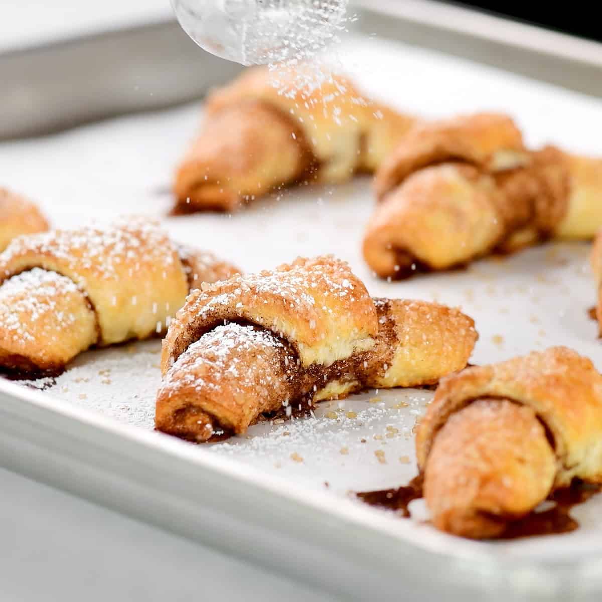 Sprinkling powdered sugar on cottage cheese cinnamon roll crescents.