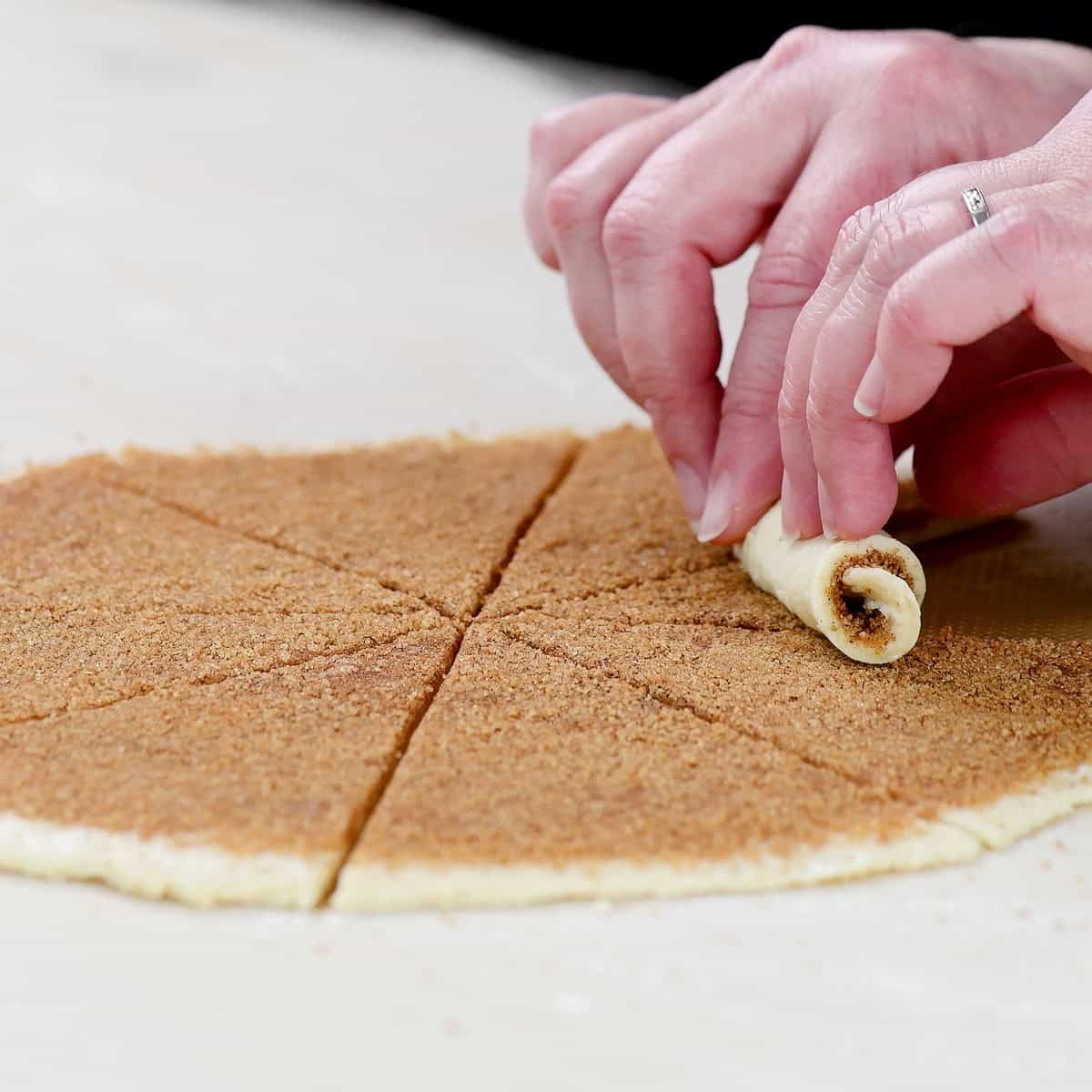 Rolling the sugar coated dough into a crescent shape.