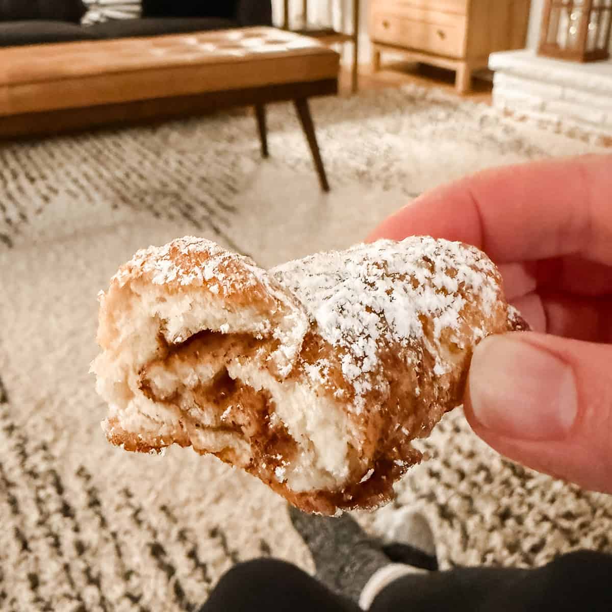 A hand holding a powdered cottage cheese cinnamon crescent roll.